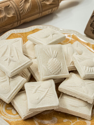 Springerle Cookies on a mustard colored plate with a springerle rolling pin and mold in the background.