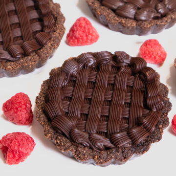 An individual Chocolate Caramel Tart on a white background with raspberries.