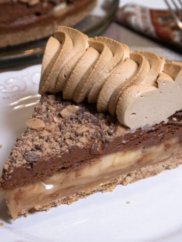 A slice of Banoffee Pie with coffee whipped cream sits on a white plate.