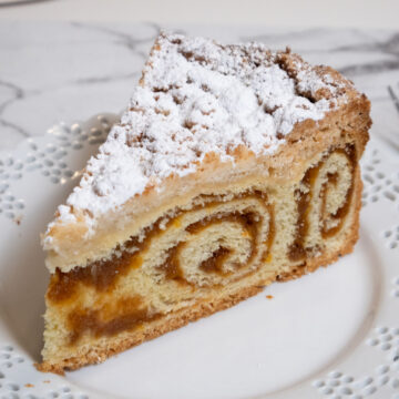 This picture shows a slice of the coffee cake on a white, lace edged plate on a marble counter.