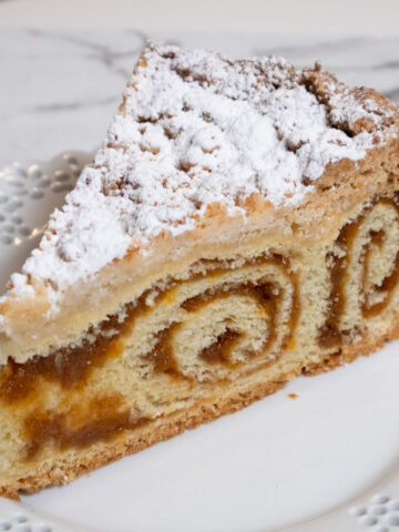 This picture shows a slice of the coffee cake on a white, lace edged plate on a marble counter.