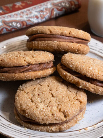 Four Peanut Butter Sandwich Cookies on a white plate with a brown rim.