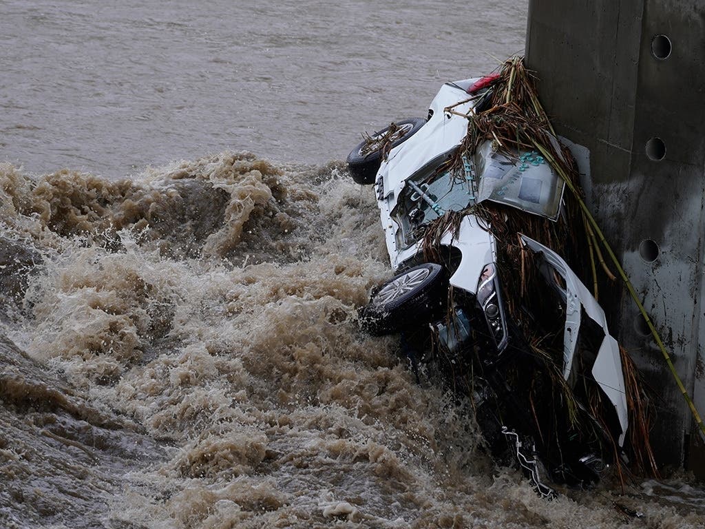 A submerged vehicle is wedged against a bridge pillar in the surging Los Angeles River making it difficult for firefighters to access it on Tuesday. The vehicle was spotted in the river before dawn.