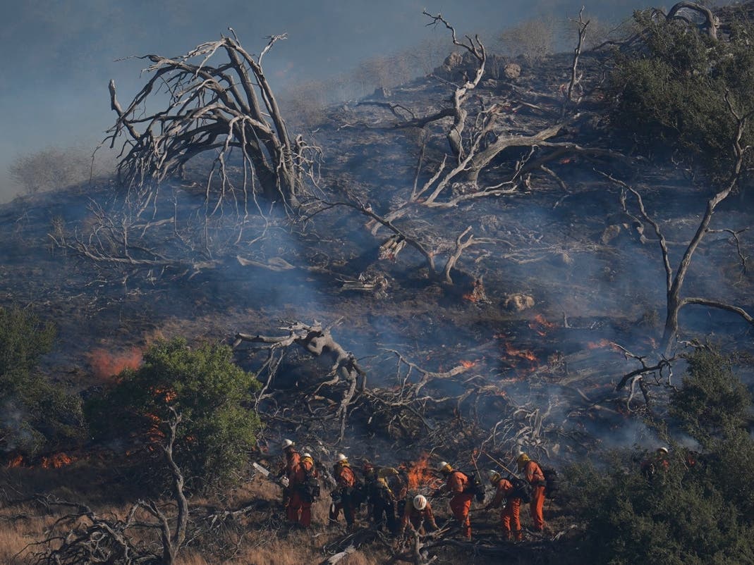 Firefighters work under a smoldering hillside left behind by the Post Fire Saturday, June 15, 2024, in Gorman, California. 