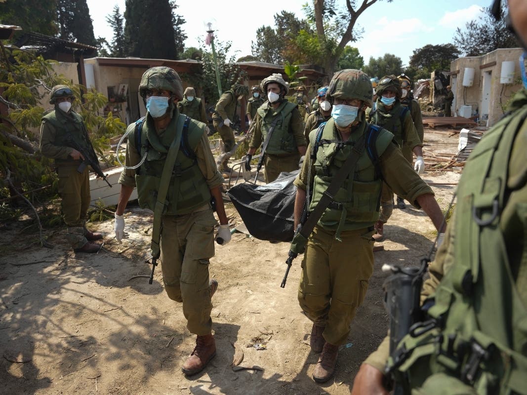 Israeli soldiers carry the body of a person killed in the Hamas attack in kibbutz Kfar Azza on Tuesday. Hamas militants overran the kibbutz on Saturday, where many Israelis were killed and taken captive.