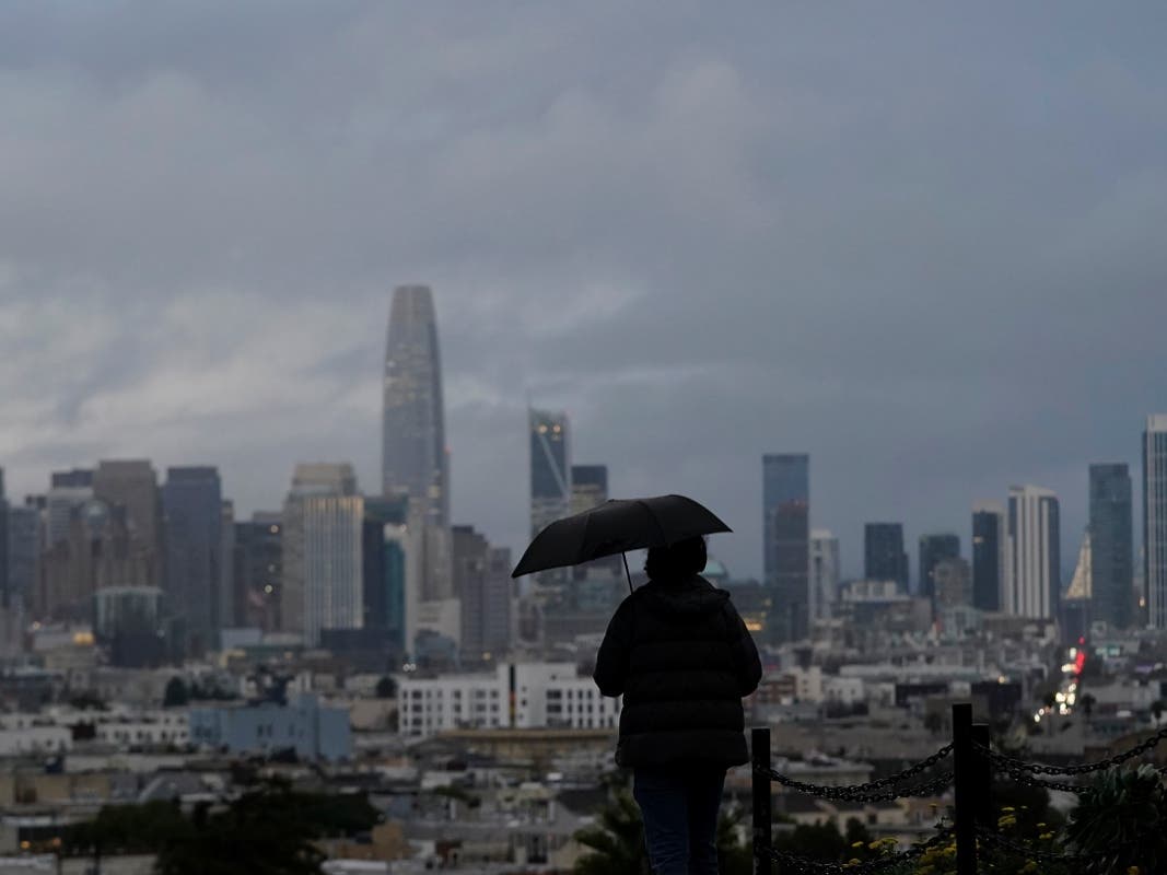 A pedestrian carries an umbrella while looking toward the skyline from Dolores Park in San Francisco on Dec. 13, 2021.