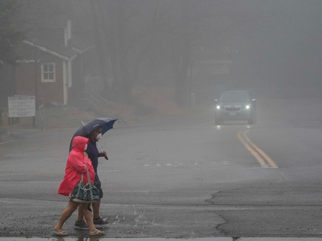 Two people cross the road as wind and rain pummel the area Friday. A tropical storm nearing Southern California has brought fierce winds, rain and the threat of flooding to a region already dealing with wildfires and an extraordinary heat wave.