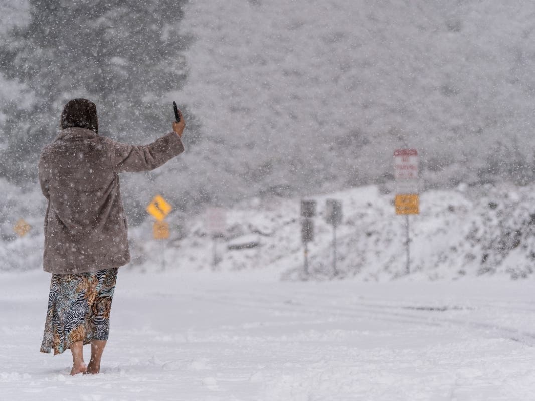 A visitor stands on a snow-covered road while taking a selfie in the Angeles National Forest near La Canada Flintridge, Calif., Thursday, Feb. 23, 2023. 