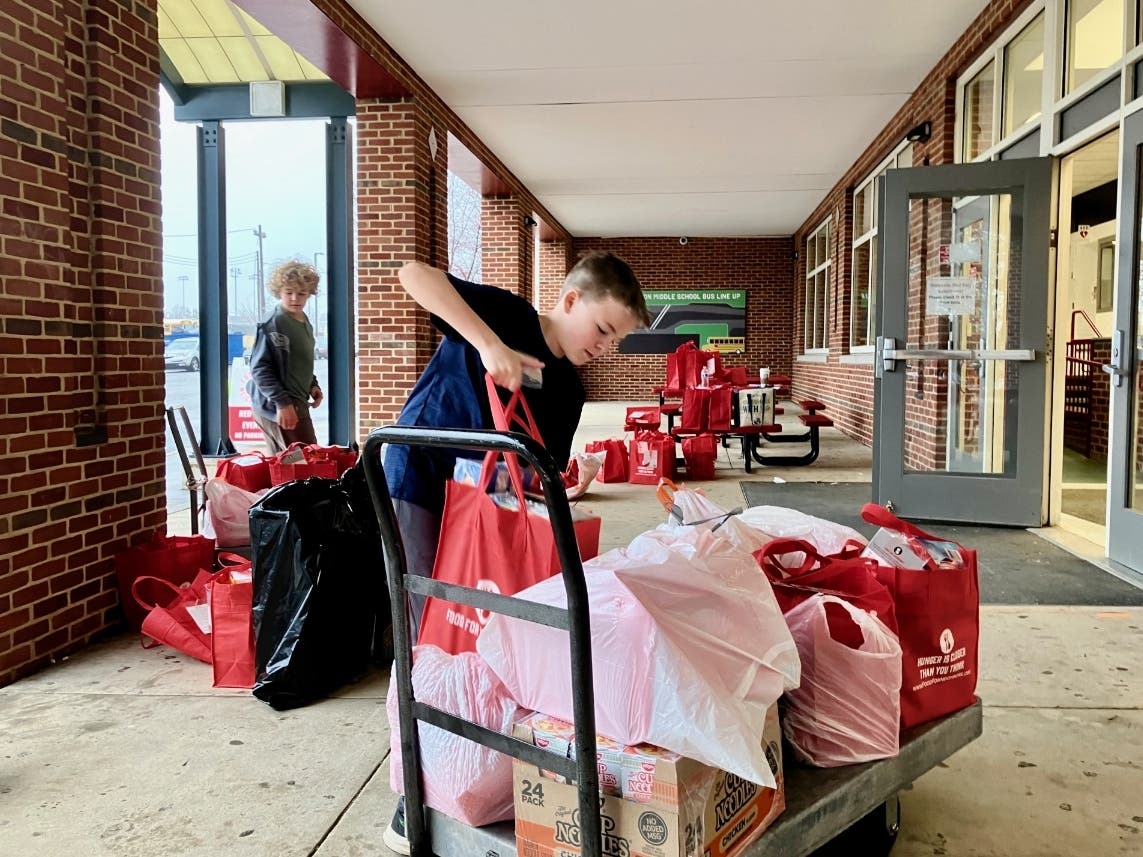 A young volunteer loads the dolly with red bags full of food and toiletries for transport to community members for unpacking and sorting. Volunteers then deliver the donations to school pantries for students in need.