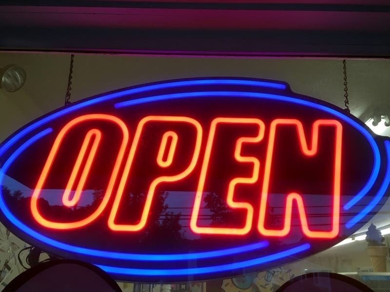 Neon 'OPEN' sign hanging on the inside of a door at a local shop.