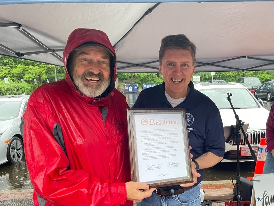 On left, John Lovaas accepts a proclamation from Hunter Mill Supervisor Walter Alcorn at the start of last Saturday's Farmers Market at Lake Anne, which Lovaas started in 1998.