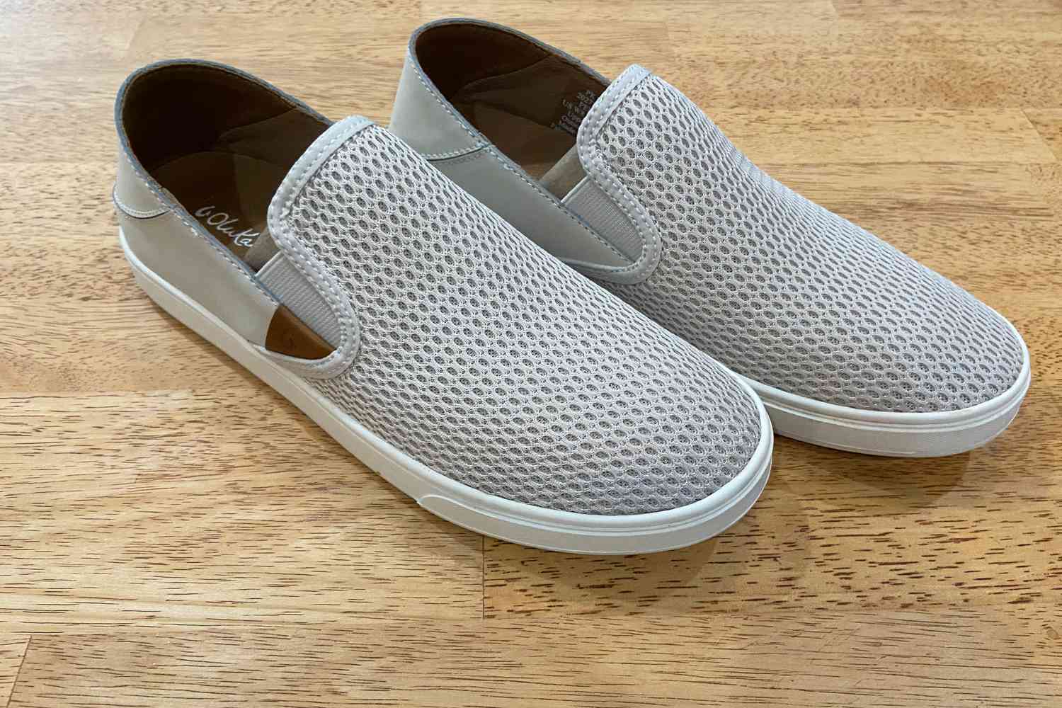 OluKai Pehuea Slip On Sneakers on a wood floor