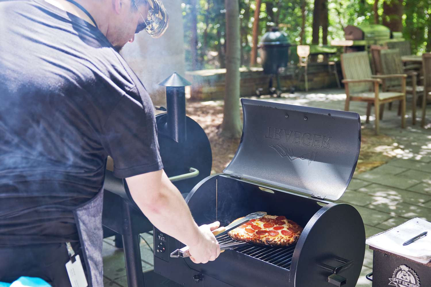 Person removing a cooked pizza from a Traeger TFB30KLF Tailgater Pellet Grill with other pellet grills alongside it