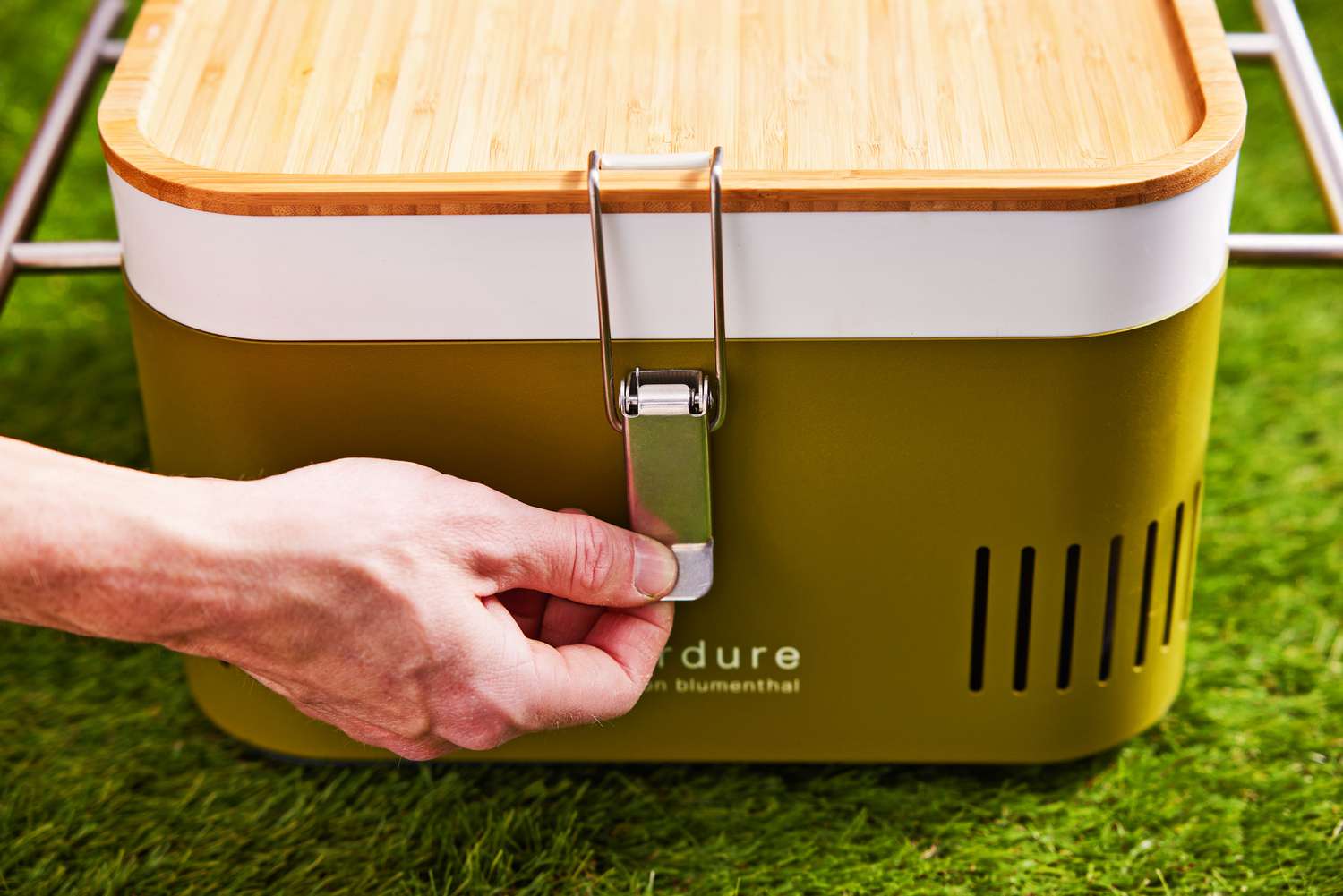 Hand closing the Everdure Cube Portable Charcoal Grill