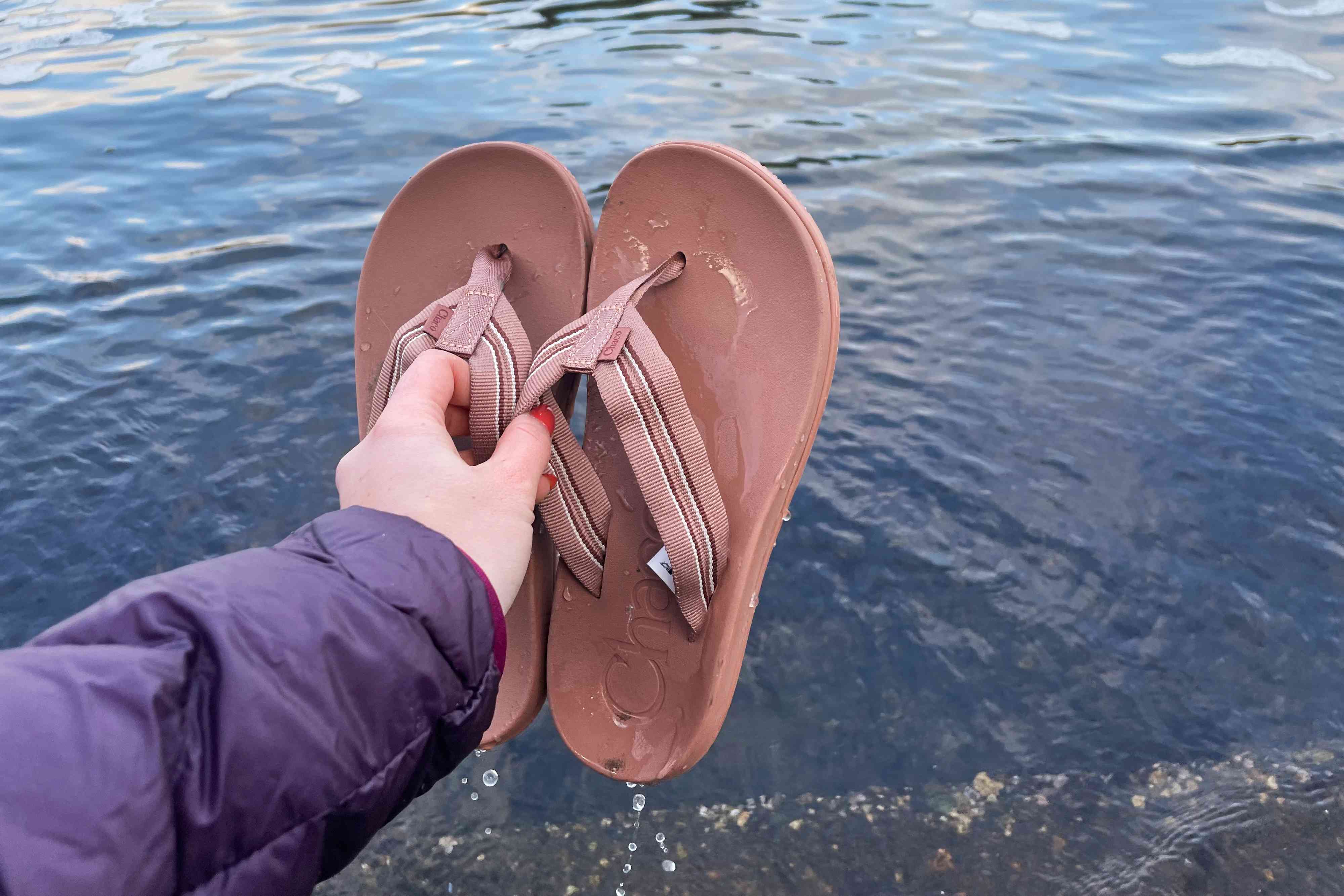 Hand holding a pair of Chaco Women's Chillos Flip Flops with water in the background 