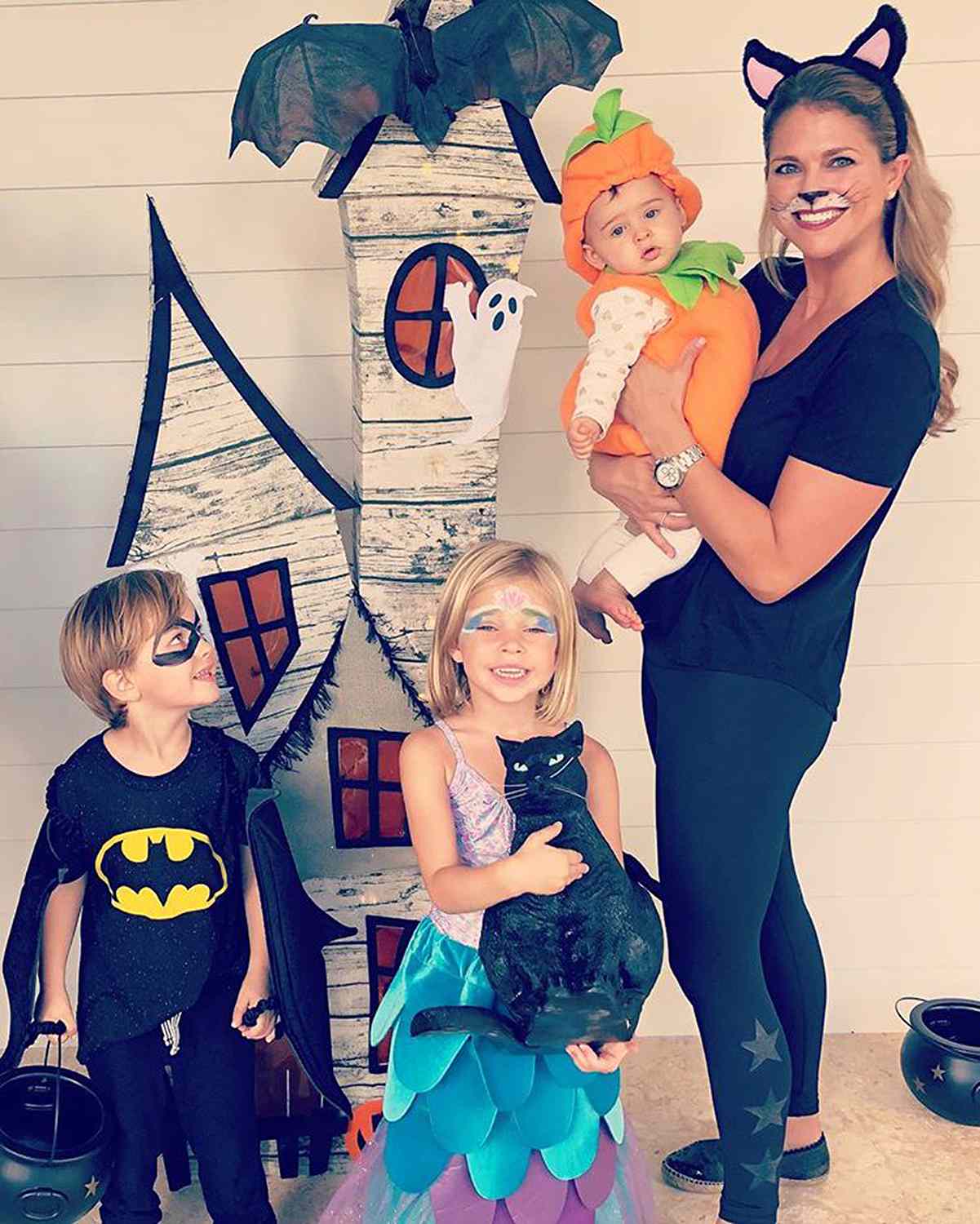 Princess Madeleine of Sweden dressed up as a classic black cat, holding Princess Adrienne dressed as a pumpkin on her first Halloween.. 