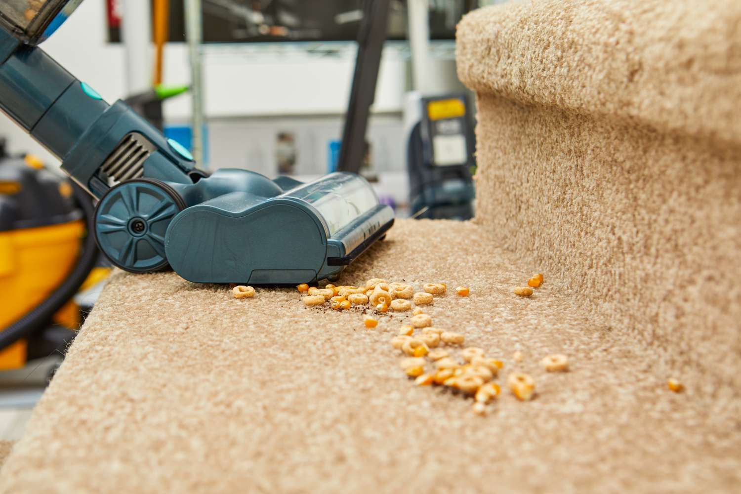 A close-up of the Belife V12 Cordless Vacuum Cleaner vacuuming cereal on carpeted stairs.