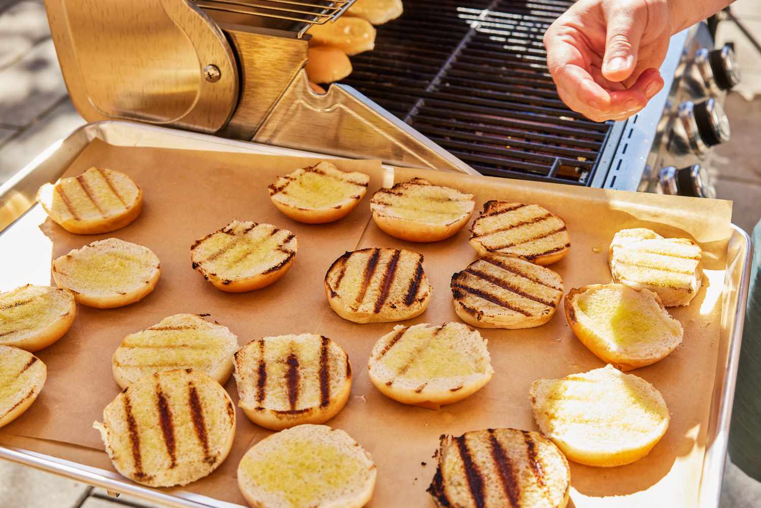 Grilled burger buns displayed on a baking sheet on the Monument Grills Stainless 4-Burner Propane Gas Grill's side table