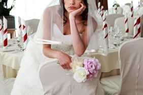 Bride sitting in a ceremony waiting restaurant. Sitting sad with head and flowers in her hands.