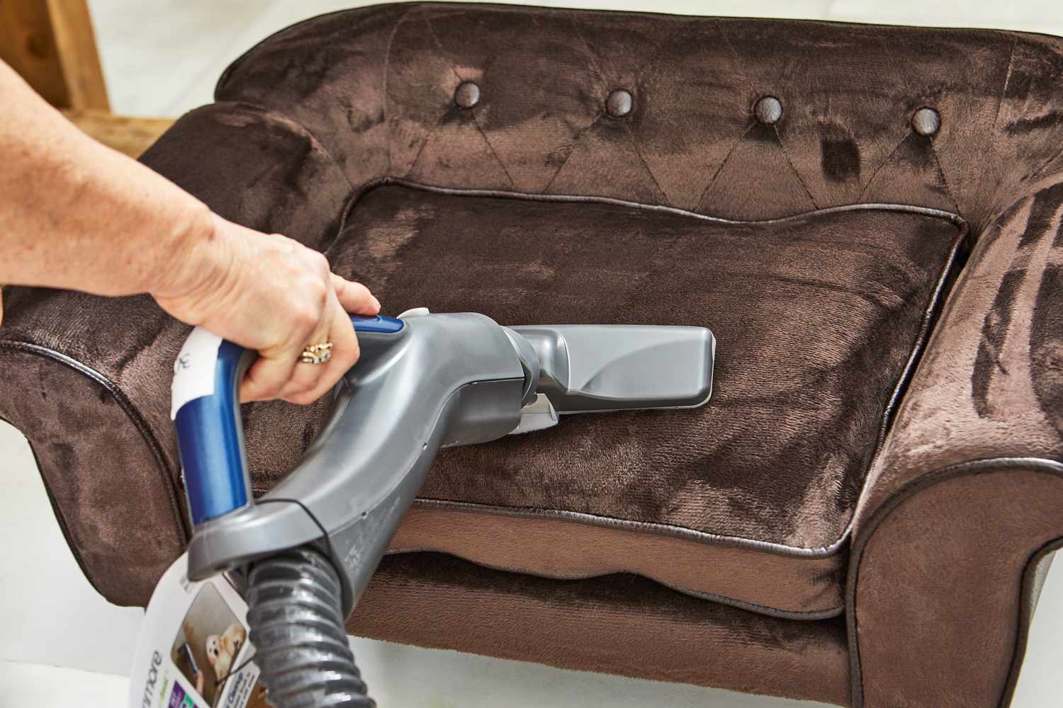 Hand using a Kenmore Pet Friendly Pop-N-Go Bagged Canister Vacuum to vacuum a brown chair