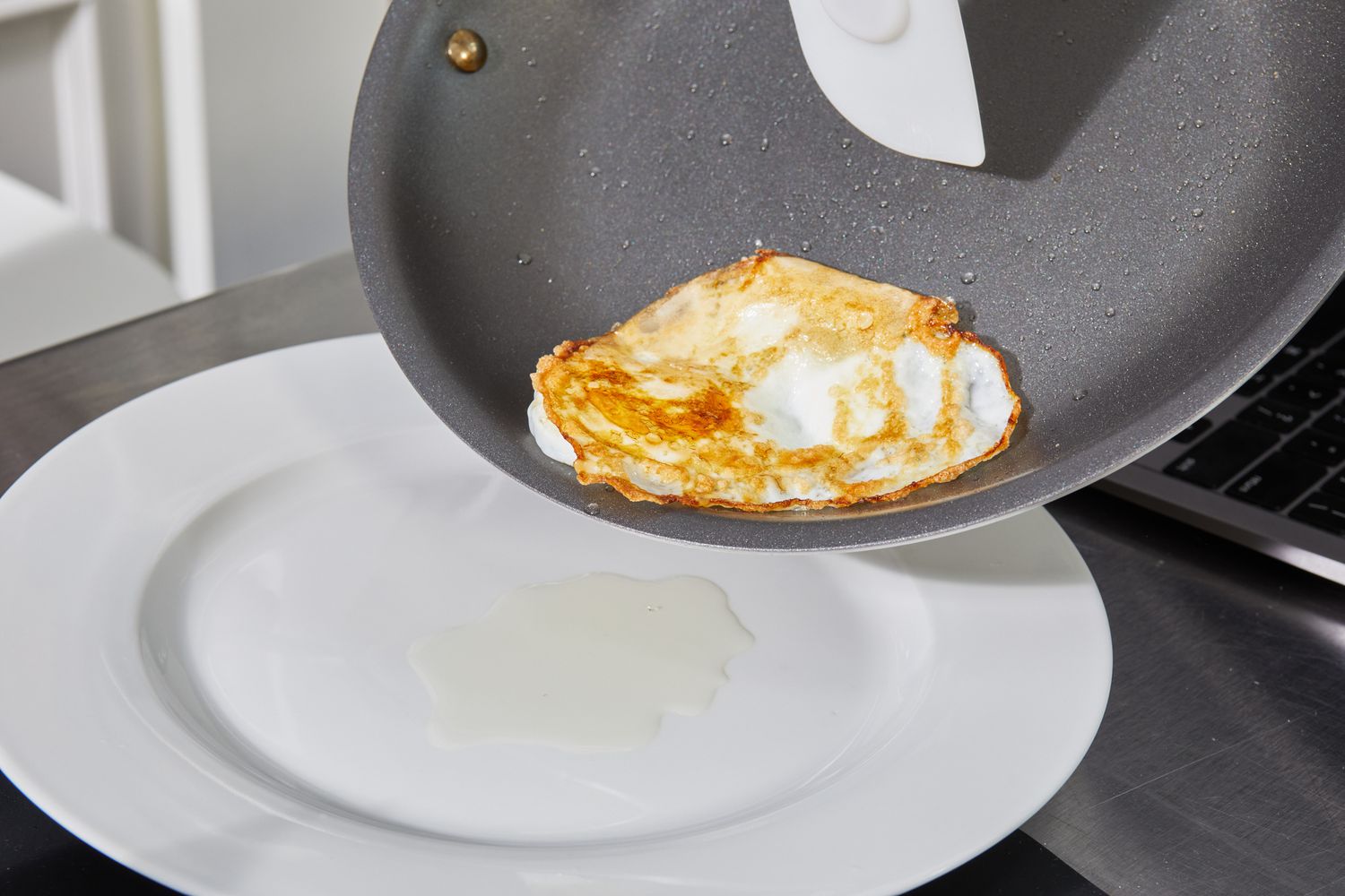 Using rubber spatula to slide over-easy egg onto white plate from Made In nonstick sauté pan