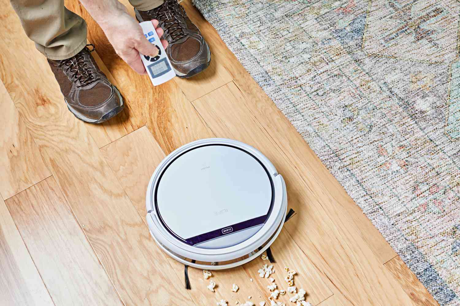 Person holding remote standing next to ILIFE V3s Pro Robot Vacuum Cleaner cleaning popcorn from floor