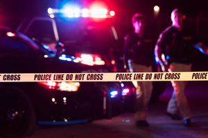 Two multi-ethnic police officers standing in front of patrol cars, behind police tape, wearing bulletproof vests and duty belts. 