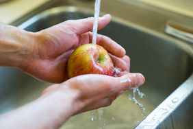 Closeup of hands holding a brightly coloured apple under the water of a faucet in a sink in the kitchen