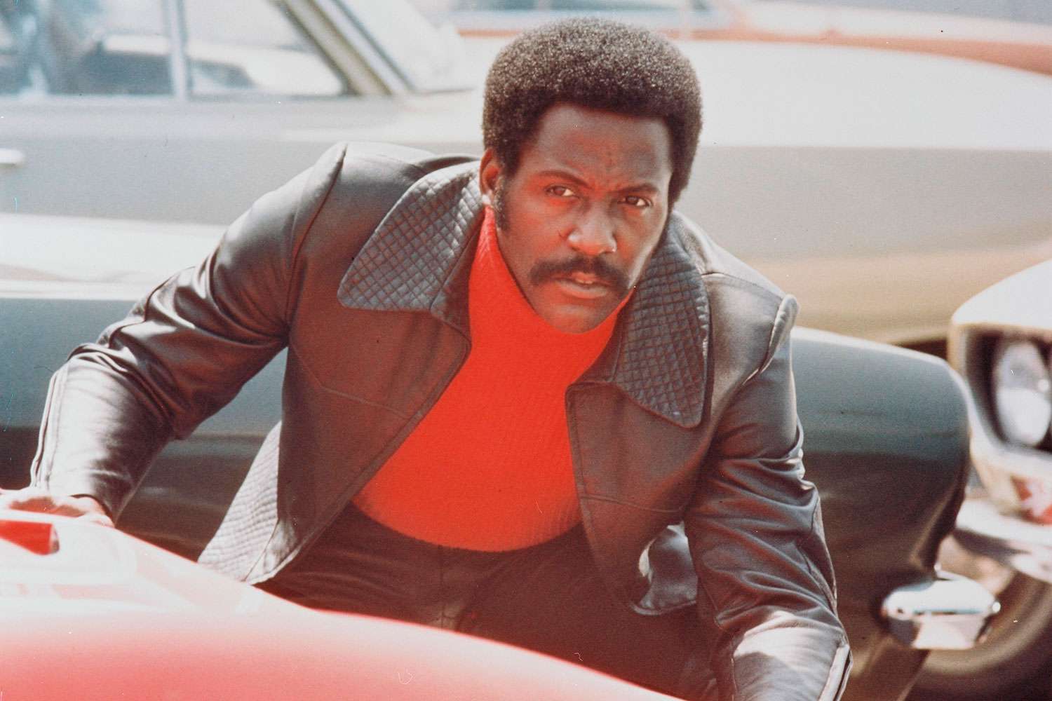 Richard Roundtree, US actor, crouching behind a red sports car in a publicity still issued for the film, 'Shaft', 1971. The blaxploitation film, directed by Gordon Parks (1912-2006), starred Roundtree as 'John Shaft'. 