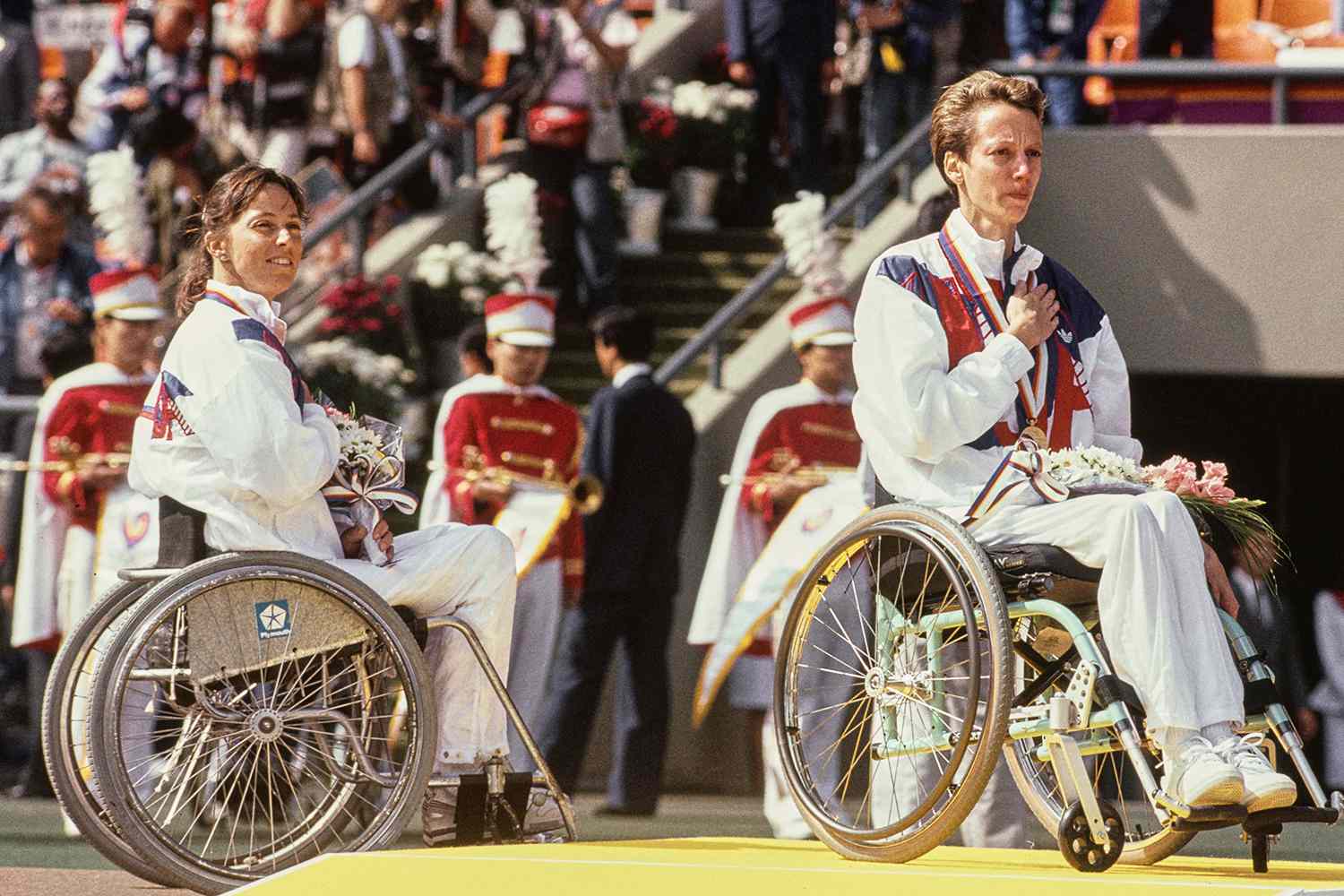 Gold medalist Sharon Hedrick from the United States with third placed bronze medalist compatriot Candace Cable during the playing of the national anthem at the awards ceremony after winning the Women's 800 metres wheelchair demonstration race at the XXIV Summer Olympic Games.