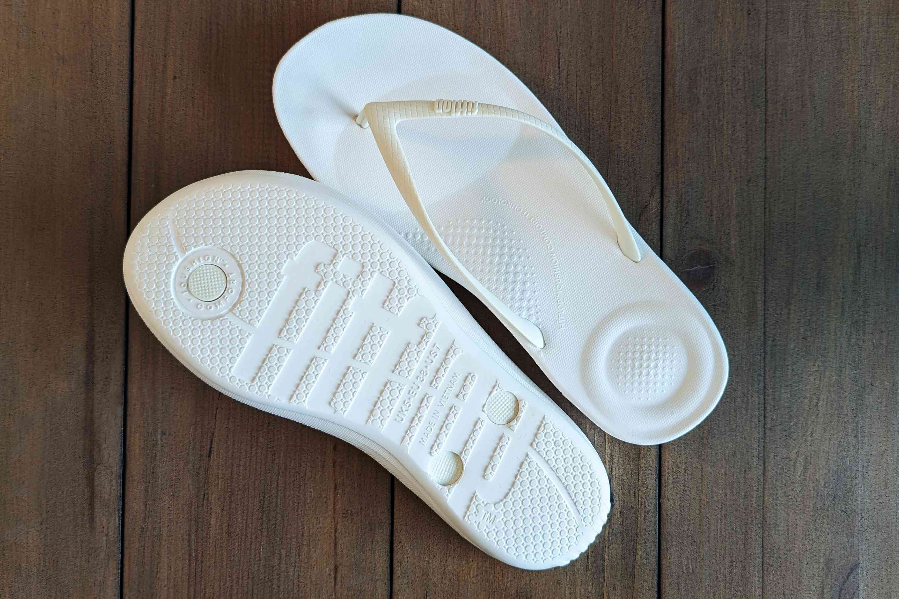 The top and bottom of the Fitflop iQushion Ergonomic Flip Flops on wood flooring 