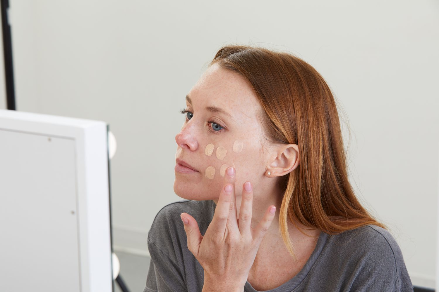 Person applying PÜR 4-in-1 Tinted Moisturizer Broad Spectrum SPF 20 while looking into mirror