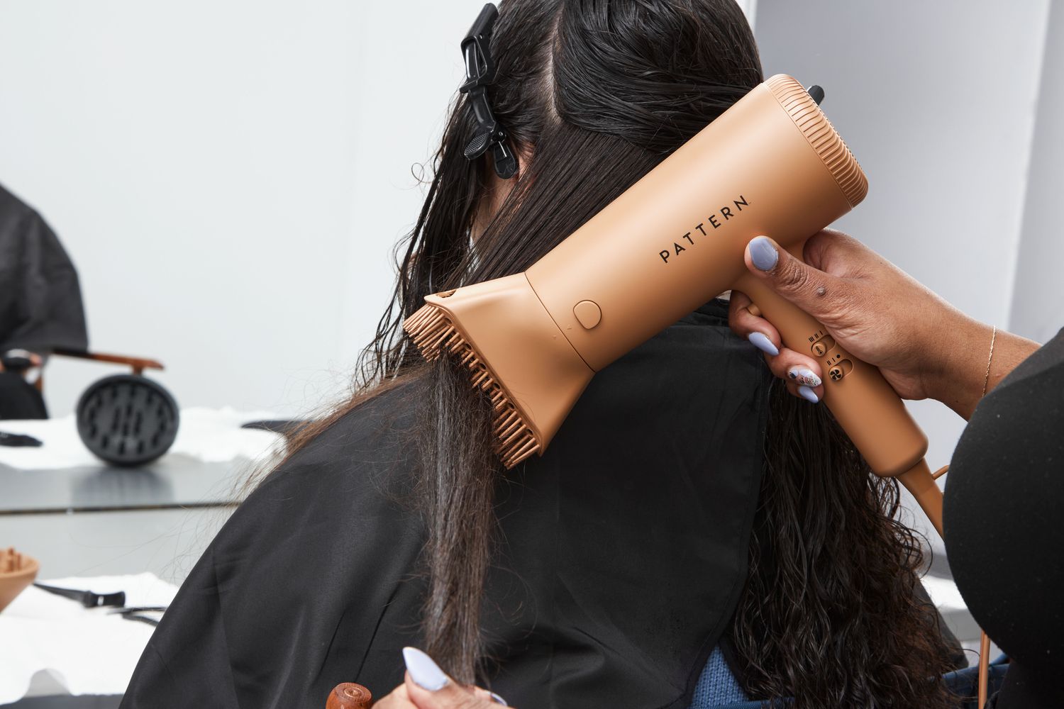 A person using one of the PATTERN Blow Dryer's accessories to dry another person's hair.