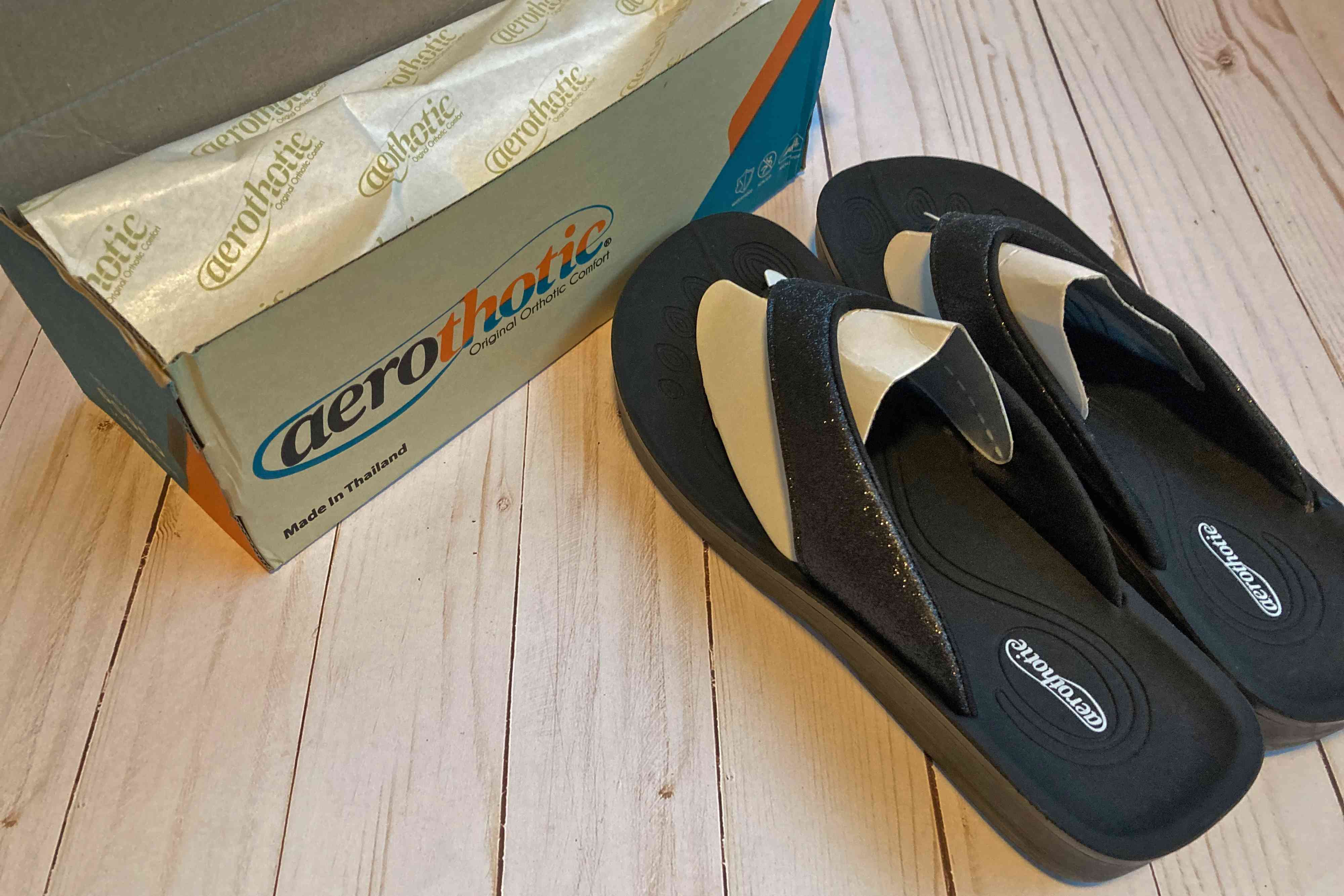 Aerothotic Orthotic Flip Flops displayed next to shoe box on wood flooring 