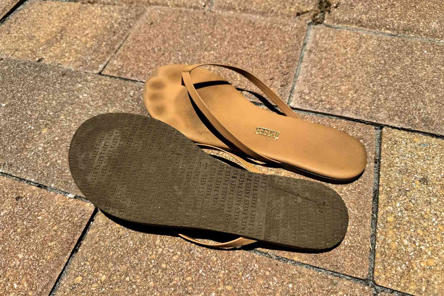 Worn Tkees Flip-Flop Sandals on ground with one flat and other flipped over to show bottom