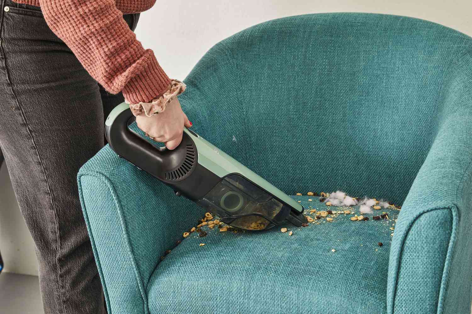 Hand using the Shark UltraCyclone Pro Cordless Handheld Vacuum to clean food from upholstered chair