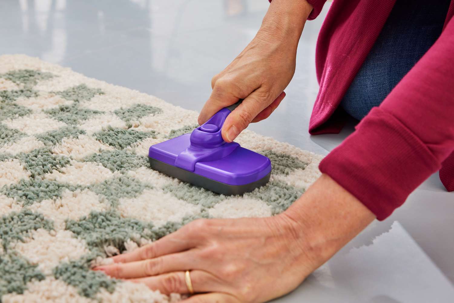 A person uses a lint brush on the AllModern Walker Checkered Shag Area Rug