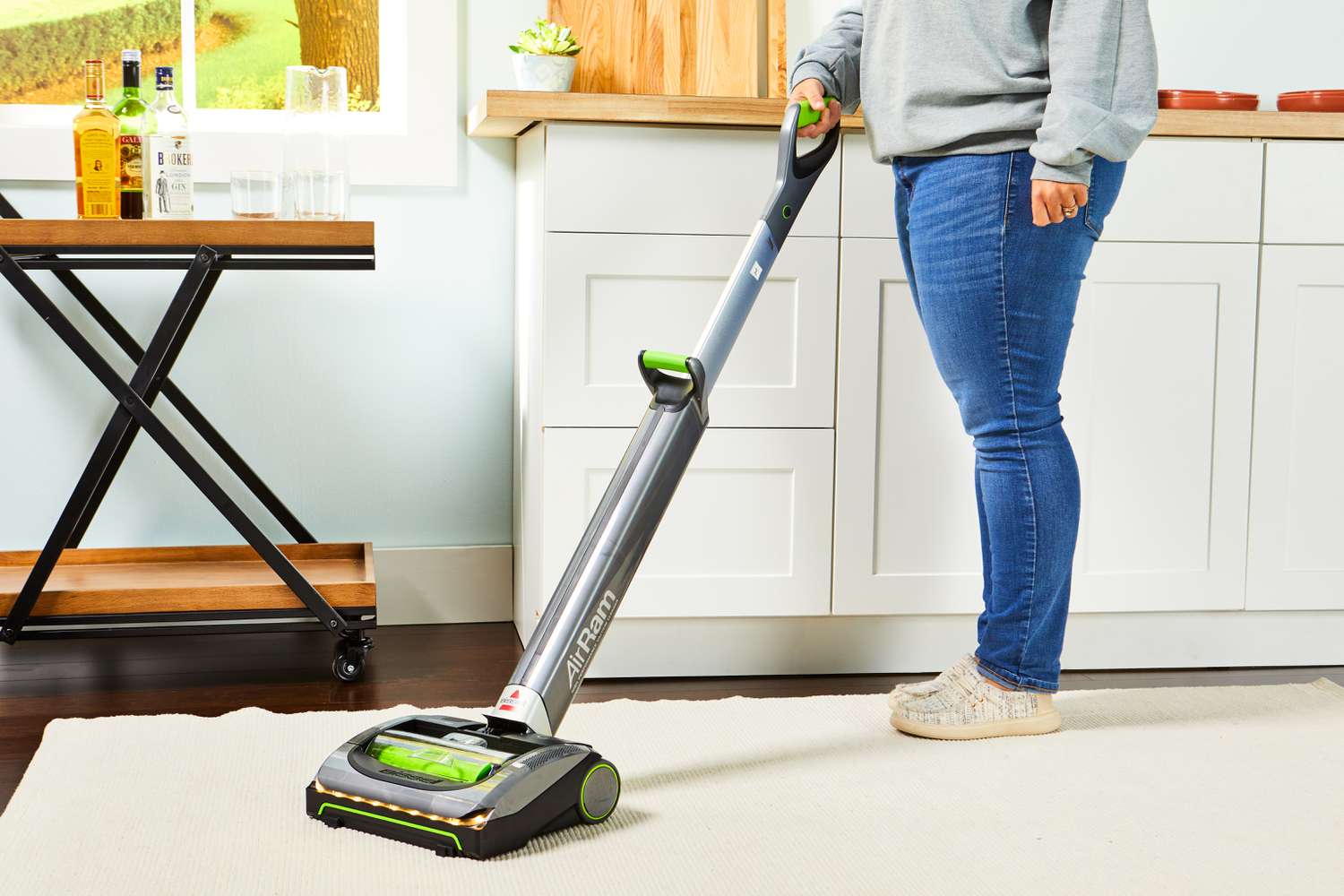 A person vacuuming a rug in a kitchen using the Bissell 1984 Air Ram Cordless Vacuum.