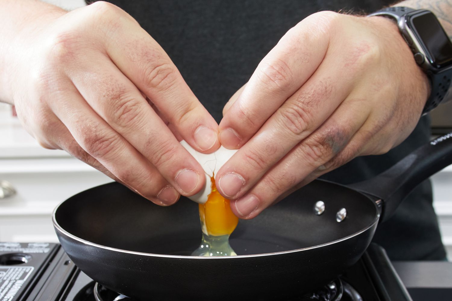 A person cracks an egg into the Farberware Dishwasher Safe Nonstick 15 Piece Cookware Pots and Pans Set pan