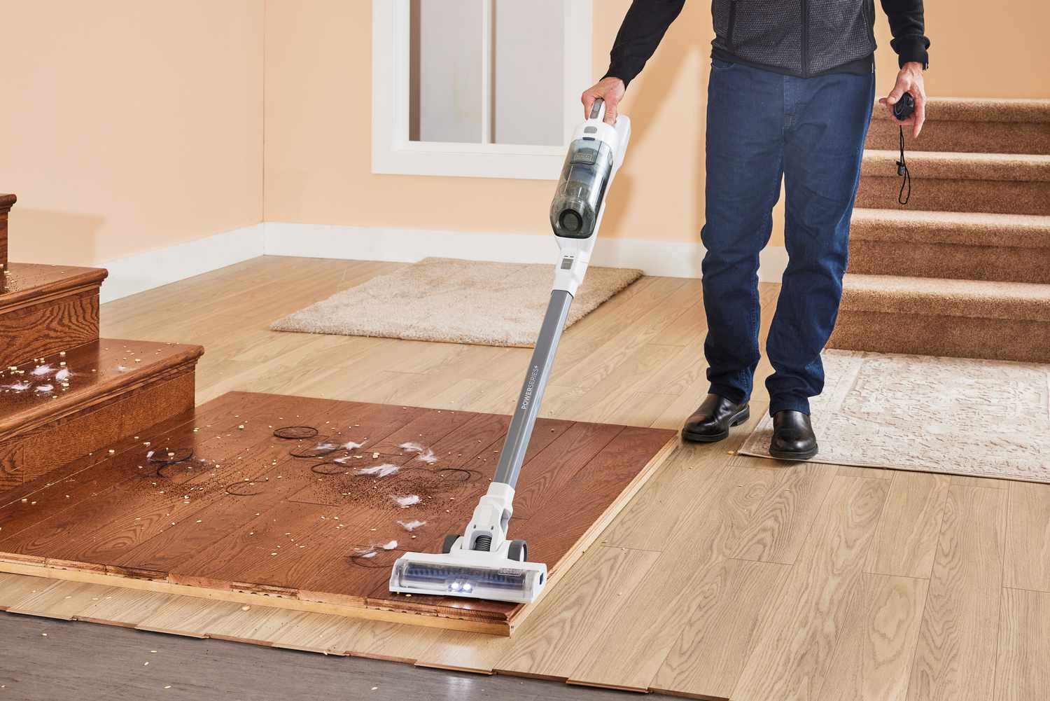 A person using the Black + Decker Powerseries+ 16V MAX Cordless Stick Vacuum to clean up a mess on wooden planks