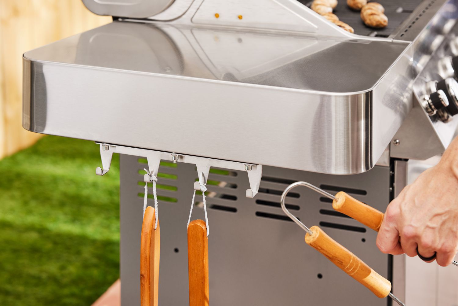 Hand hanging tongs on a hook on the side of the Monument Grills Stainless 4-Burner Propane Gas Grill