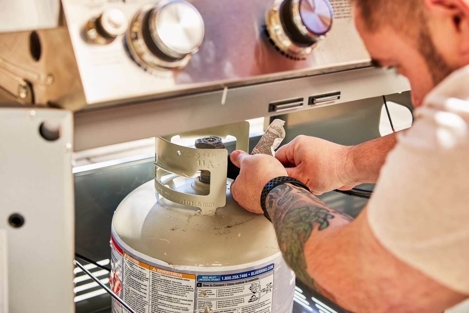 Person attaching a propane tank to the Monument Grills Stainless 4-Burner Propane Gas Grill