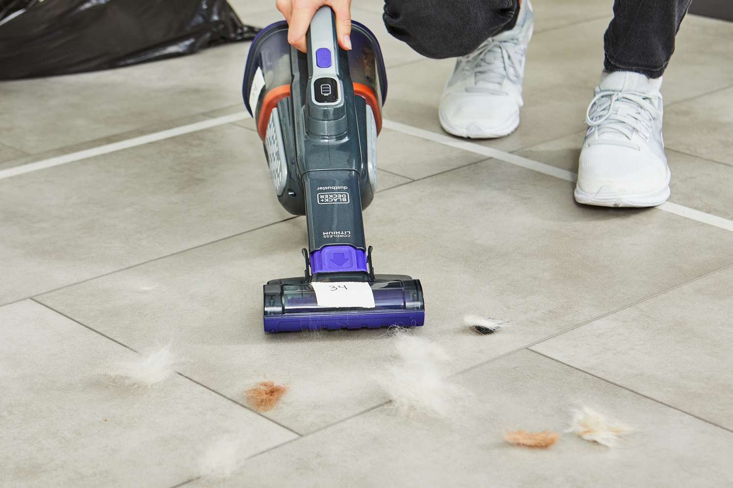 Hand using the Black+Decker Dustbuster AdvancedClean+ Pet Cordless Hand Vacuum Cleaner to clean pet hair from a tile floor