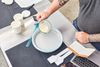 Person pouring the ice cream liquid from a measuring cup into the Chef'n Sweet Spot Ice Cream Maker displayed on a stainless steel surface