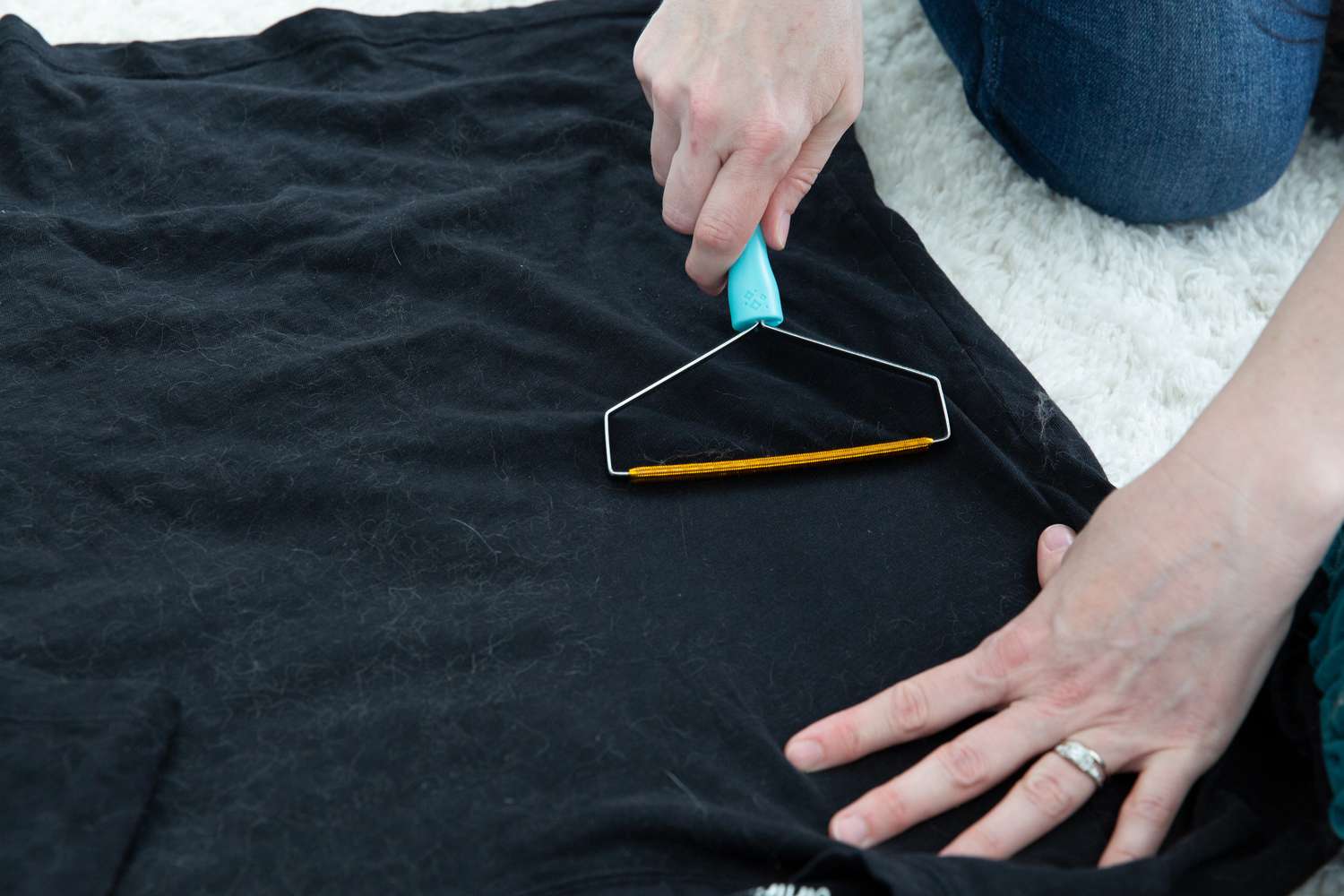 Hands using a Uproot Cleaner Pro Reusable Pet Hair Remover to clean fur off a black shirt