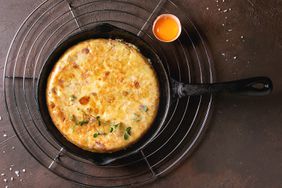 Spanish potato omelette tortilla with bacon served in cast-iron pan on cooling rack with egg yolk and salt over over dark brown texture background Top view, space. (Photo by: Natasha Breen/REDA&CO/Universal Images Group via Getty Images)