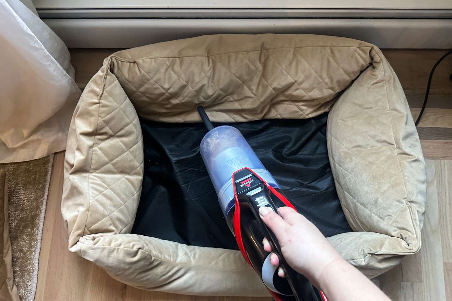 A person uses the Bissell CleanView Pet Slim Corded Stick Vacuum to clean a dog bed