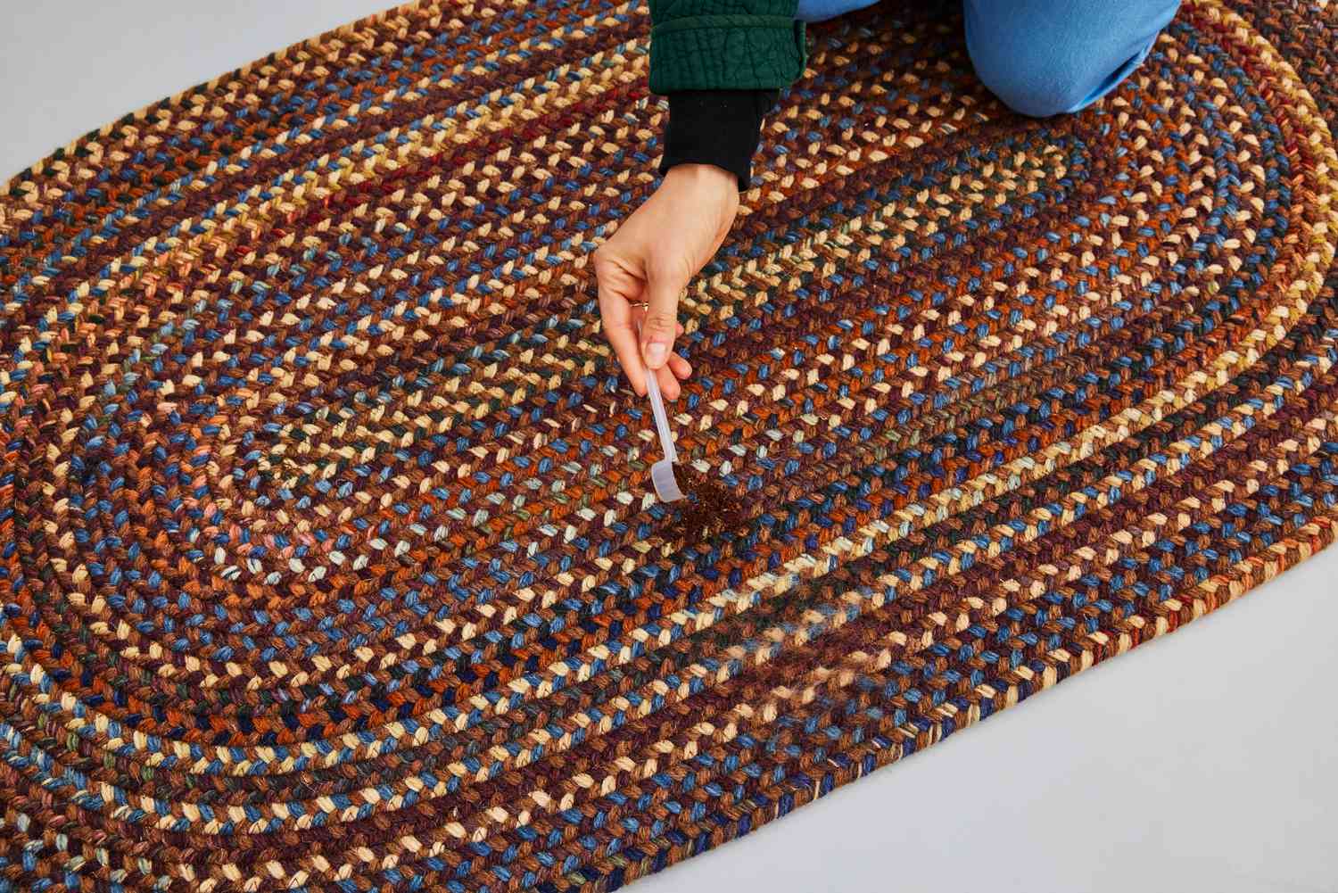 A person drops dirt onto the L.L.Bean Braided Wool Rug, Oval