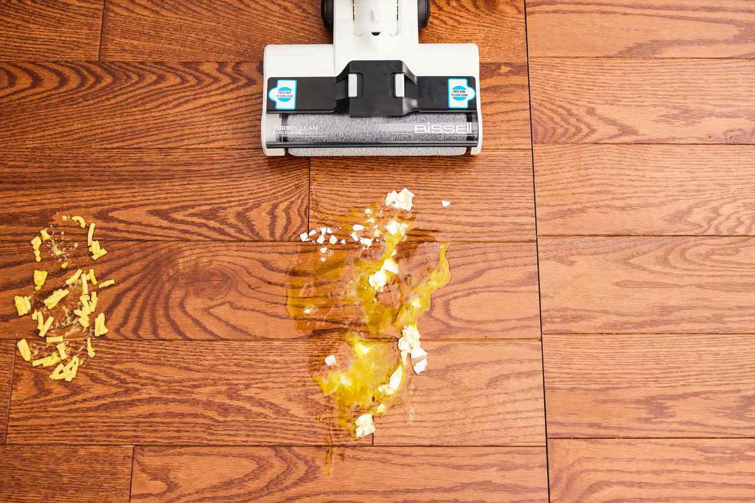 The Bissell TurboClean Cordless Hard Floor Cleaner is used to clean up a dropped egg from a wood floor