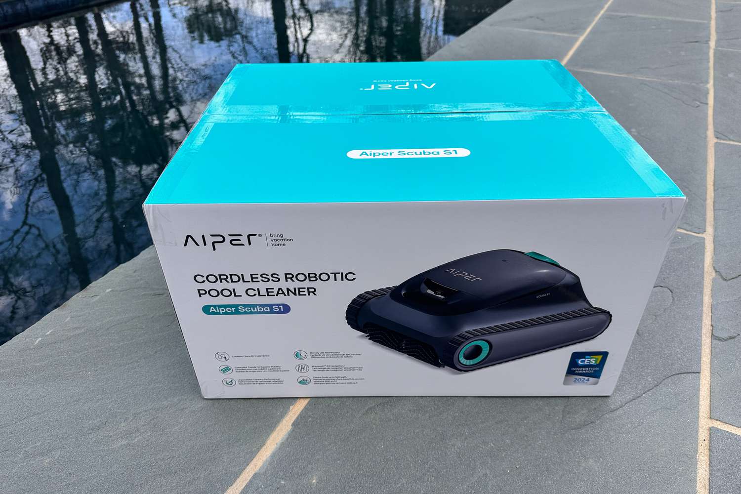 The Aiper Scuba S1 Pool Cleaner in the box at the edge of a pool